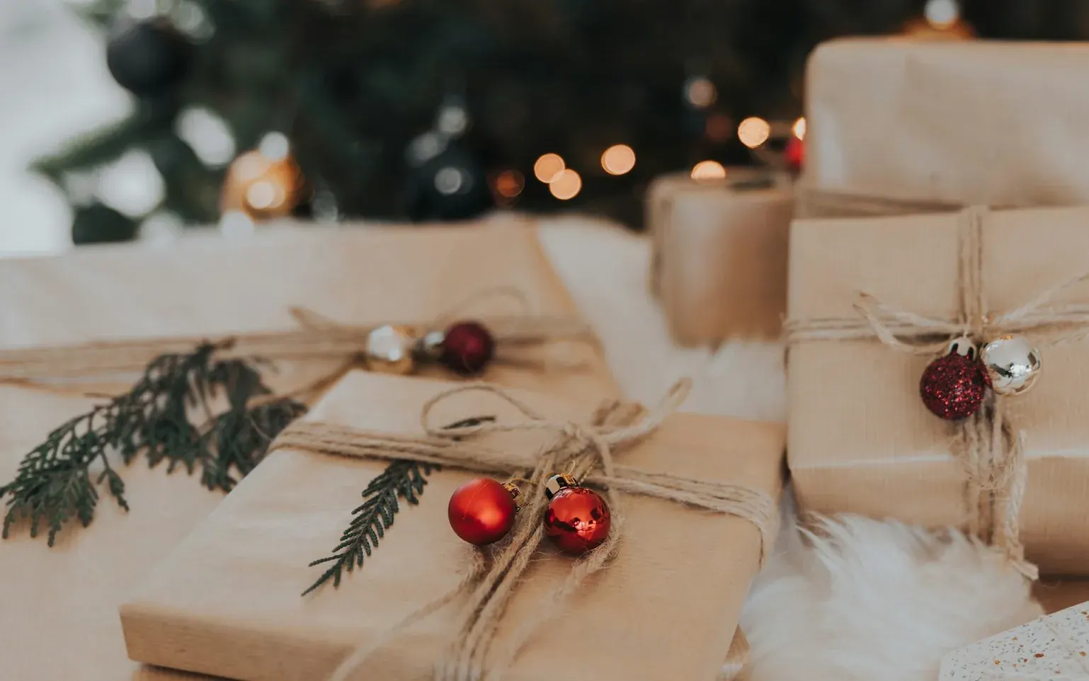 Regalos envueltos en papel kraft con cordel y bolas rojas, delante del árbol de Navidad